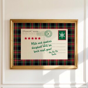 May include: A framed Christmas postcard with a gold frame and a plaid border. The postcard reads "Milk and cookies sleighed! Will be back next year!" with a Santa signature and a snowflake stamp.