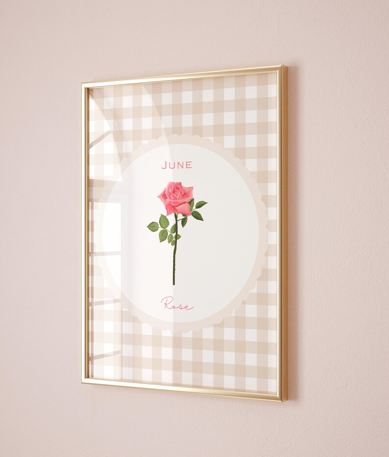 May include: Framed print featuring a pink rose illustration. The artwork is set against a beige and white gingham pattern, with the words "June" and "Rose" displayed. The frame is gold.