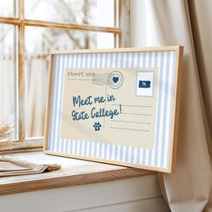 May include: A framed postcard with a light blue and white striped border. The postcard features the text "Meet me in State College!" and a paw print. A stamp with "PA" is in the upper right corner.