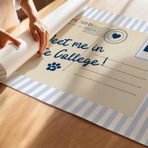 May include: A rolled-up poster with a vintage postcard design. The postcard features the text "Meet me in State College!" in navy blue script, a paw print, and a heart-shaped stamp. The border has blue and white stripes.