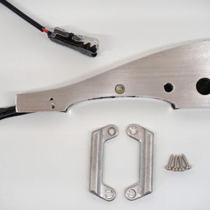 Può includere: Un assortimento di componenti hardware metallici, tra cui un pezzo curvo in alluminio spazzolato con fori multipli, due pezzi a forma di staffa e un piccolo mucchio di viti. È presente anche un cavo nero con un connettore.