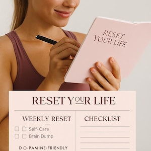 Puede incluir: Una persona sostiene un diario rosa con el texto "RESET YOUR LIFE". La imagen muestra un diario abierto con páginas rayadas y una lista de verificación. También se ve el texto "DESIGNED FOR FOCUS. BUILT FOR YOUR ROUTINE".