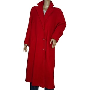 May include: A long, pillar-box red coat with a classic design. The coat features a wide collar, button closure, and long sleeves. The coat is displayed on a mannequin, showcasing its full length and tailored fit. A timeless outerwear piece.