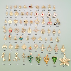 May include: A collection of gold-toned metal charms in various shapes including animals, plants, symbols, and playing cards, each labeled with a unique identification number from 291 to 359, arranged in a grid pattern on a light background.