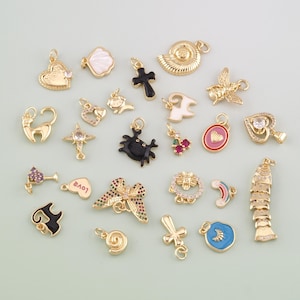 Op de afbeelding: Een verzameling goudkleurige bedels met diverse ontwerpen, waaronder harten, kruisen, een kat, een krab, een strik en een regenboog. Sommige bedels hebben kleurrijke emaille accenten. Deze kleine hangers zijn voor het maken van sieraden.