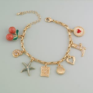 May include: Gold-toned charm bracelet featuring various charms, including a red cherry, a starfish, a heart, and a seashell. The bracelet has a lobster clasp closure and is approximately 7 inches in length.