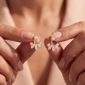 Peut inclure: Une paire de boucles d'oreilles de type ear jacket dorées, composées d'une pierre ronde transparente en haut et d'un élément en éventail en bas, orné de cinq pierres transparentes taille marquise disposées en éventail.