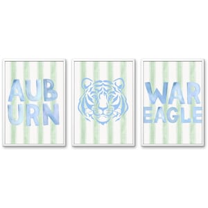 May include: A set of three framed wall art prints featuring light green vertical stripes on a white background. The first print displays the blue text AUBURN, the second shows a blue tiger face illustration, and the third shows the blue text WAR EAGLE.