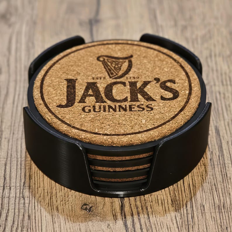May include: A set of round cork coasters with the text "Jack's Guinness" and a harp logo, held in a black holder. The coasters are made of natural cork material and are designed to protect surfaces from drink condensation.