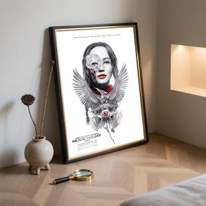 May include: Framed poster for "The Hunger Games: Mockingjay - Part 1". The artwork features a woman with a rose over one eye, red lipstick, and a stylized bird with outstretched wings. The poster is in a black frame.