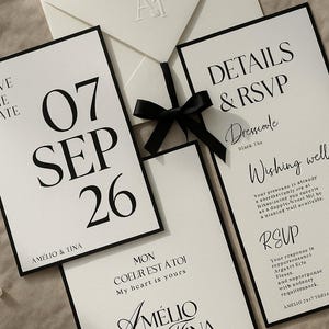 Puede incluir: Elegante juego de invitaciones de boda en blanco y negro. Incluye un sobre, una tarjeta de guardar la fecha, una tarjeta de confirmación de asistencia y una tarjeta de detalles. Las tarjetas muestran la fecha "07 SEP 26" y los nombres "AMÉLIO & TINA".