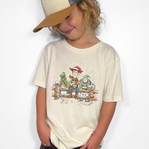 Puede incluir: Camiseta color crema con una ilustraci&oacute;n festiva de Woody, Buzz Lightyear y Rex de Toy Story, todos con gorros de Pap&aacute; Noel. El dise&ntilde;o est&aacute; ambientado en un fondo de valla nevada, perfecto para la temporada navide&ntilde;a.