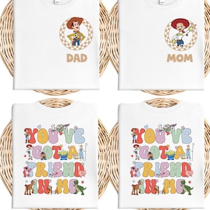 May include: Four white t-shirts with colorful graphics. Two shirts have character portraits and the words "DAD" and "MOM." The other two shirts say "YOU'VE GOT A FRIEND IN ME" with cartoon characters.