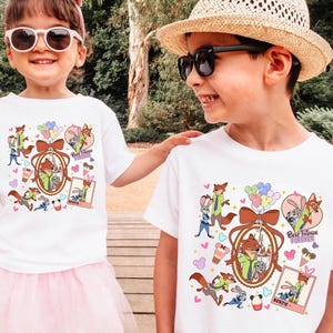 Może przedstawiać: Dwoje dzieci w białych koszulkach z kolorowym wzorem z kresk&oacute;wek. Wz&oacute;r zawiera postacie z kresk&oacute;wek, balony oraz napisy "Best Friends Forever" i "Bestie". Dziewczynka ma na sobie r&oacute;żową tutu i okulary przeciwsłoneczne.