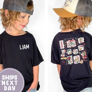 Puede incluir: Camiseta negra con el nombre "LIAM" en blanco en la parte delantera. La parte posterior de la camiseta presenta un gráfico colorido con temática navideña con personajes de dibujos animados. El niño lleva una gorra de camionero con visera marrón y malla gris.
