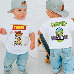 May include: White t-shirt with a graphic design featuring the number "3" in a cowboy-themed design, with the text "YOU'VE GOT A FRIEND IN ME" and "THREE". The back of the shirt has the name "DAVID" and a Buzz Lightyear-themed "3".