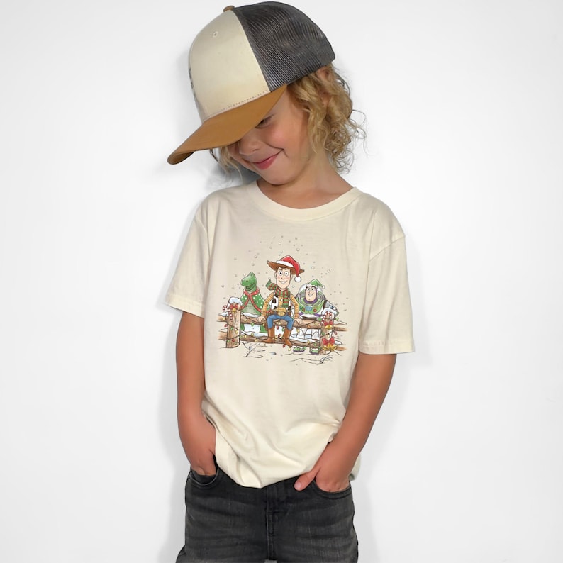 Puede incluir: Camiseta color crema con una ilustraci&oacute;n festiva de Woody, Buzz Lightyear y Rex de Toy Story, todos con gorros de Pap&aacute; Noel. El dise&ntilde;o est&aacute; ambientado en un fondo de valla nevada, perfecto para la temporada navide&ntilde;a.