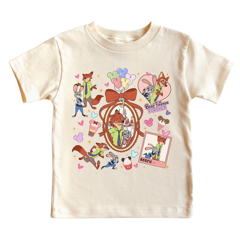 Może przedstawiać: Kremowa koszulka z postaciami z kresk&oacute;wki Zootopia. Projekt zawiera Nicka Wilde'a i Judy Hopps, a także tekst "Best Friends Forever" i "Bestie". Grafika zawiera r&oacute;wnież serca, rożki lod&oacute;w i balony.