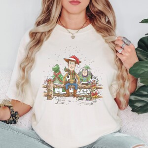 Puede incluir: Camiseta color crema con una ilustraci&oacute;n festiva de Woody, Rex y Buzz Lightyear de Toy Story. Woody lleva un gorro y bufanda de Pap&aacute; Noel, Rex un jersey navide&ntilde;o. El dise&ntilde;o incluye una valla nevada y detalles de bastones de caramelo.