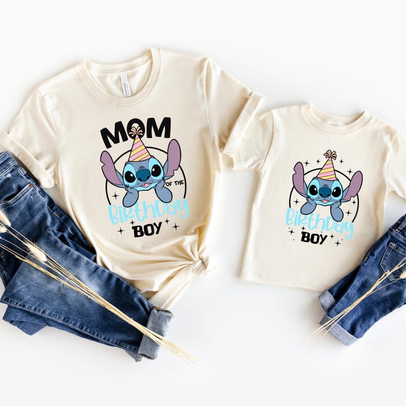 K&ouml;nnte beinhalten: Zwei cremefarbene T-Shirts mit einem Cartoon-Charakter-Design. Auf einem Shirt steht "MOM OF THE BIRTHDAY BOY" und auf dem anderen "BIRTHDAY BOY". Beide Shirts haben eine blaue Cartoon-Figur mit Partyhut.
