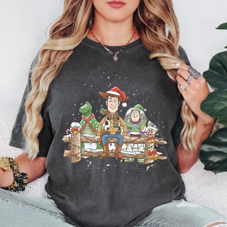 Puede incluir: Camiseta gris oscuro con un dise&ntilde;o festivo de los personajes de Toy Story: Woody, Rex y Buzz Lightyear. Woody lleva un gorro de Pap&aacute; Noel y est&aacute; sentado en una valla de madera. El dise&ntilde;o incluye nieve y decoraciones navide&ntilde;as.