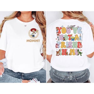 May include: White t-shirt featuring a cartoon image of a cowgirl with the word "Mommy" in brown on the front. The back of the shirt has the phrase "You've Got a Friend in Me" with cartoon characters.