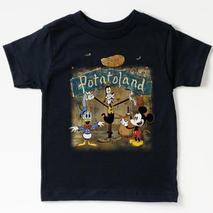 May include: Navy blue t-shirt featuring a vintage-style graphic of Mickey Mouse, Donald Duck, and Goofy in front of a sign that reads "Potatoland." The design has a retro cartoon aesthetic.