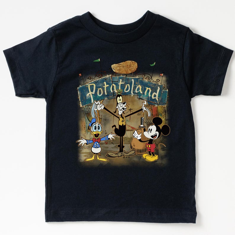 May include: Navy blue t-shirt featuring a vintage-style graphic of Mickey Mouse, Donald Duck, and Goofy in front of a sign that reads "Potatoland." The design has a retro cartoon aesthetic.