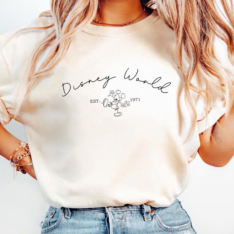 May include: Cream-colored sweatshirt with the words "Disney World" in a cursive font. Below the text is a line drawing of Mickey Mouse and the text "EST. 1971". The sweatshirt has long sleeves.