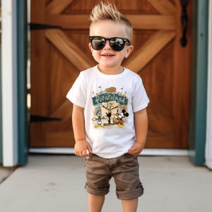 May include: A white t-shirt with the text "Potatoland" and cartoon characters Mickey Mouse and Donald Duck. The child is wearing brown shorts and black sunglasses. The background is a wooden door.