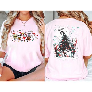 K&ouml;nnte beinhalten: Hellrosa T-Shirt mit festlichem Aufdruck. Die Vorderseite zeigt Charaktere mit Weihnachtsm&uuml;tzen und Lichterketten. Die R&uuml;ckseite zeigt einen Weihnachtsbaum mit Jack Skellington und Zero. Ein skurriles Urlaubsdesign.