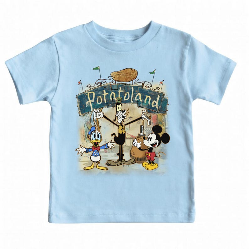 May include: Light blue toddler t-shirt featuring a colorful graphic of Disney characters Mickey Mouse, Donald Duck, and Goofy in front of a sign that reads "Potatoland". The design includes a potato and green flags.
