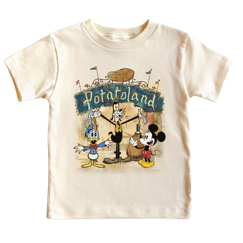 May include: Cream-colored toddler t-shirt featuring a colorful graphic of Disney characters Donald Duck, Goofy, and Mickey Mouse. The graphic includes the text "Potatoland" above the characters. The shirt has short sleeves and a crew neck.