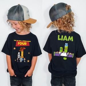 May include: A child wearing a black t-shirt with a Toy Story graphic and the text "YOU'VE GOT A FRIEND WHOS FOUR". The back of the shirt has the name "LIAM" and a Buzz Lightyear design. The child is also wearing a gray and tan baseball cap.