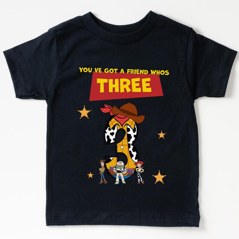 May include: Navy blue t-shirt with a graphic featuring the number "3" designed as a cowboy with a hat and bandana. The shirt includes the text "YOU'VE GOT A FRIEND WHOS THREE" and images of cartoon characters and stars.