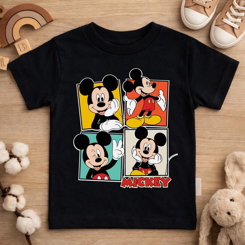 May include: Black short-sleeved t-shirt featuring a four-panel design of Mickey Mouse in various poses. Each panel has a different colored background. The word "MICKEY" is printed in red and white at the bottom.