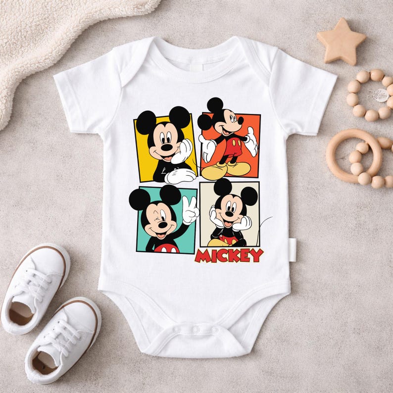 May include: White baby bodysuit featuring four panels with different poses of Mickey Mouse. The word "Mickey" is printed in red at the bottom. The bodysuit is surrounded by baby shoes, a wooden star, and a teething ring.