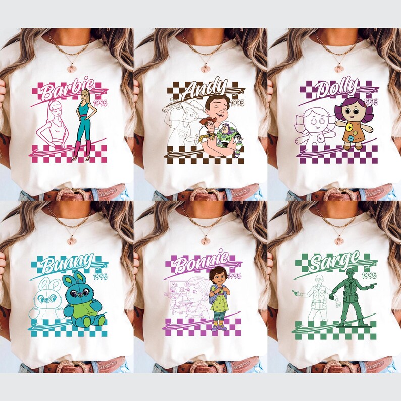 Op de afbeelding: Zes cr&egrave;mekleurige t-shirts met verschillende grafische ontwerpen. Elk shirt heeft een personagenaam, zoals "Barbie" of "Andy", met een bijbehorende illustratie en het jaartal "1996" in een geblokte kader. De ontwerpen zijn in verschillende kleuren.