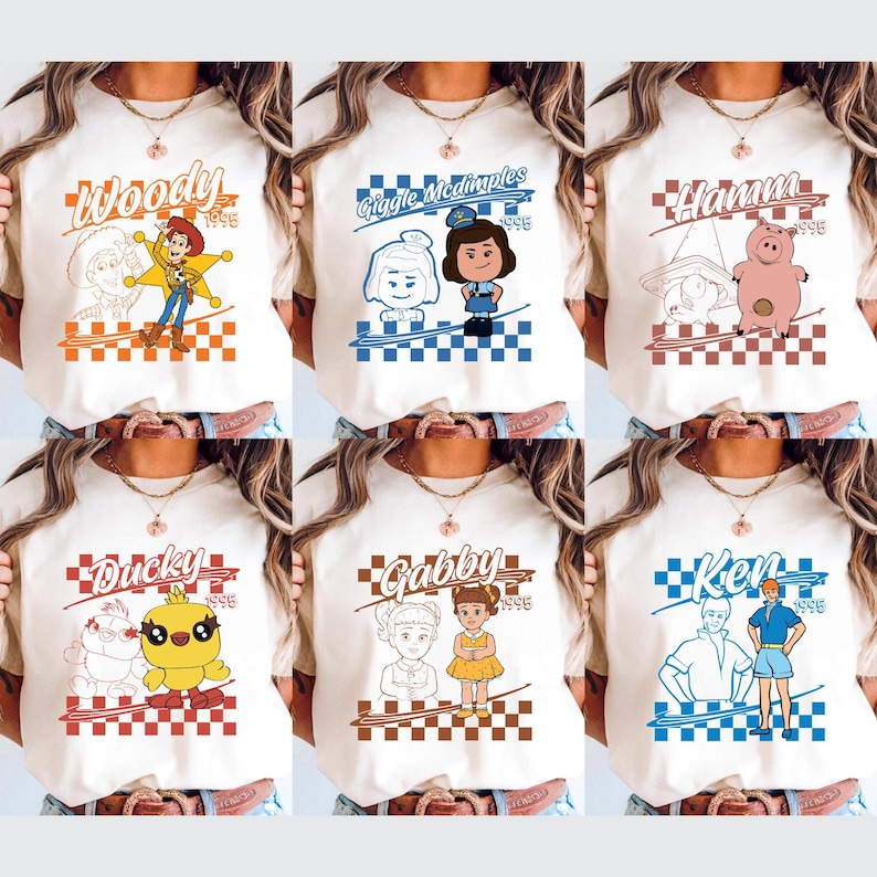 Op de afbeelding: Cr&egrave;mekleurige T-shirts met verschillende Toy Story-personages. Elk shirt heeft de naam van een personage en een grafisch ontwerp met een dambordpatroon. Personages zijn onder meer Woody, Giggle McDimples, Hamm, Ducky, Gabby en Ken.