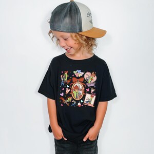 Może przedstawiać: Czarny t-shirt z postaciami z kresk&oacute;wek i napisem "Besties Forever". Str&oacute;j zawiera czapkę typu trucker z szarą siatką z tyłu, brązowym daszkiem i napisem "Love is wild".