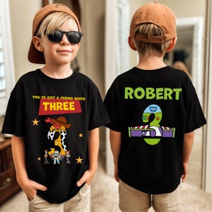 May include: Black t-shirts with a birthday theme. The front shirt has the text "YOU'VE GOT A FRIEND WHOS THREE" with a cartoon graphic. The back shirt has the name "ROBERT" and a graphic of the number 3.