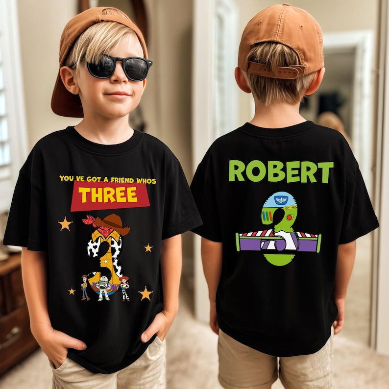 May include: Black t-shirts with a birthday theme. The front shirt has the text "YOU'VE GOT A FRIEND WHOS THREE" with a cartoon graphic. The back shirt has the name "ROBERT" and a graphic of the number 3.