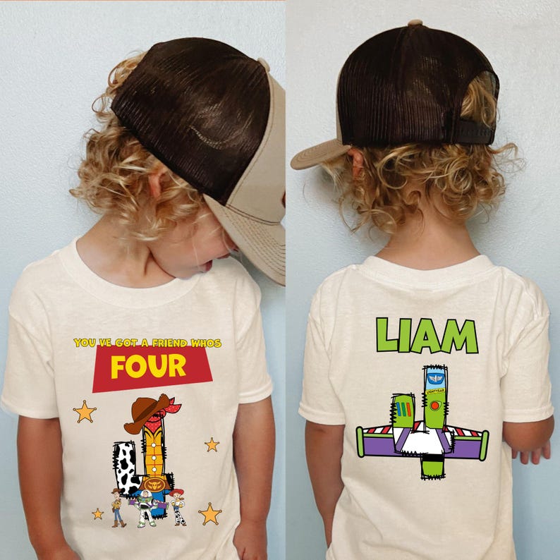 May include: A child wearing a white t-shirt with a colorful graphic featuring the text "YOU'VE GOT A FRIEND WHO'S FOUR" and a cartoon cowboy. The back of the shirt has the name "LIAM" and a Buzz Lightyear graphic.