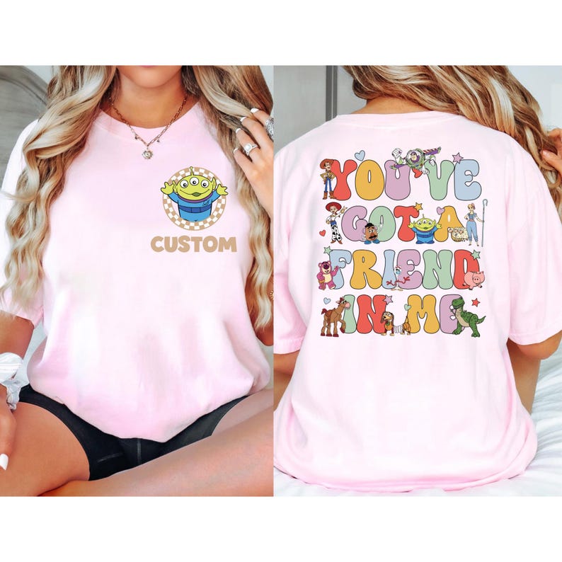 May include: Pink t-shirt featuring a cartoon alien character on the front with the word "CUSTOM" below. The back of the shirt displays the phrase "YOU'VE GOT A FRIEND IN ME" with various cartoon characters. A fun and colorful design.
