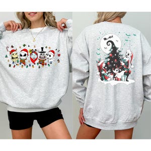 K&ouml;nnte beinhalten: Ein hellgraues Sweatshirt mit einem festlichen Design aus einem beliebten Animationsfilm. Auf der Vorderseite sind Charaktere mit Weihnachtsm&uuml;tzen und einer Lichterkette zu sehen. Auf der R&uuml;ckseite ist ein Weihnachtsbaum mit Charakteren und einem Vollmond abgebildet.