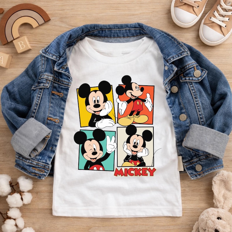 May include: White t-shirt featuring four panels of Mickey Mouse in different poses, set against yellow, red, and teal backgrounds. The word "MICKEY" is printed in red. The shirt is paired with a blue denim jacket and tan sneakers.