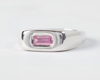 May include: A polished silver-tone ring featuring a single rectangular pink gemstone set horizontally in the center. The band has a smooth, rounded profile with a recessed setting that holds the faceted pink stone securely in place.