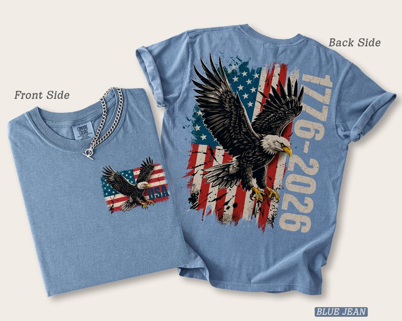 Pode incluir: Uma t-shirt azul jeans mostrada de frente e de costas. A frente apresenta um pequeno gr&aacute;fico de uma &aacute;guia sobre uma bandeira americana e o texto USA. As costas exibem uma &aacute;guia grande, uma bandeira americana desgastada e o texto 1776-2026.