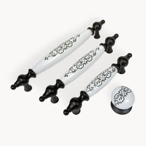 May include: A set of three white and black cabinet pulls and a matching knob. The white ceramic pulls have a black floral design and are paired with black metal hardware. The knob has a similar design.