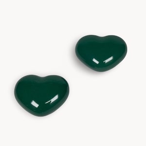 Può includere: Due oggetti lucidi a forma di cuore verde scuro su sfondo bianco. I cuori hanno una superficie liscia e riflettente, con riflessi che suggeriscono una fonte di luce. Gli oggetti sono probabilmente decorativi o gioielli.